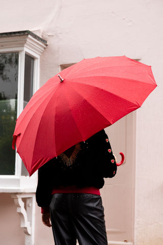 The Red Heart Umbrella shown from the back with a model standing outside a house. 