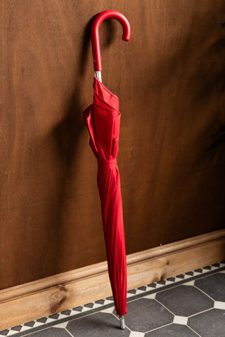 The Red Heart Umbrella shown closed and leaning against a wooden wall. 