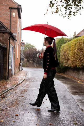 The Red Heart Umbrella shown with a model wearing black and red, on the street in the rain. 