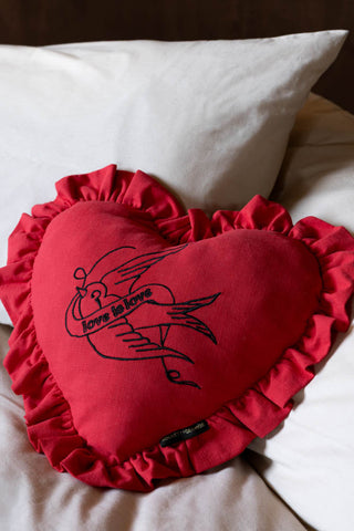 The Red Love Heart Cushion With Ruffles shown on a bed against off-white bed linen. 