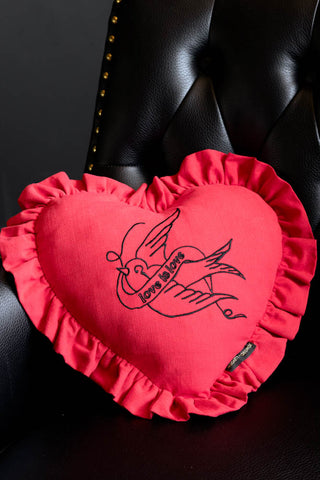 The Red Love Heart Cushion With Ruffles shown against a black leather armchair. 