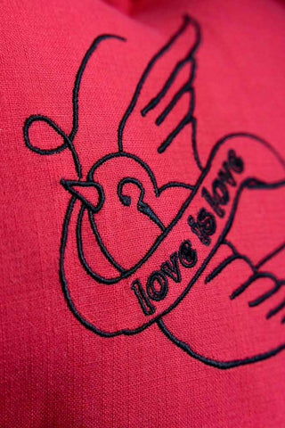 The bird and love banner embroidery in black against the red of the Red Love Heart Cushion With Ruffles. 
