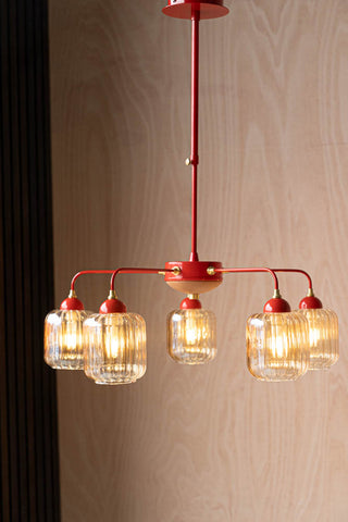 Lifestyle image of the Red Metal & Ribbed Glass Ceiling Light hanging in front of a wooden wall. 