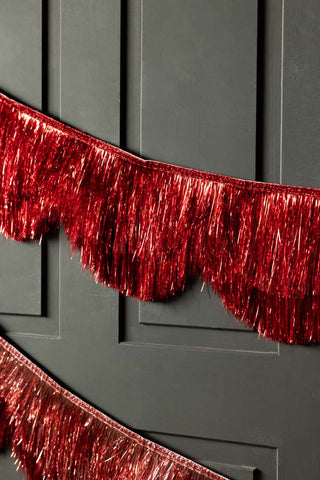The Red Scalloped Tinsel Garland styled on a black panelled wall.