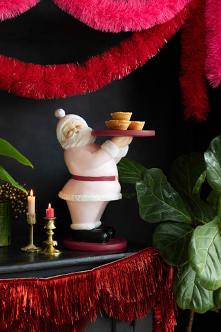 The Red Scalloped Tinsel Garland styled on the edge of a fireplace, with various other Christmas accessories surrounding it.