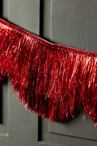 Close-up of the Red Scalloped Tinsel Garland on a black panelled wall.