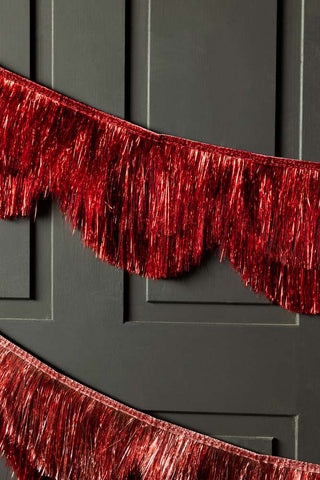 The Red Scalloped Tinsel Garland styled on a black background.
