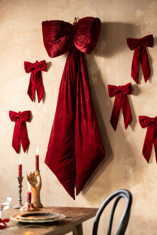 The Red Velvet Bow Christmas Decoration styled with various others and an oversized bow on a wall.