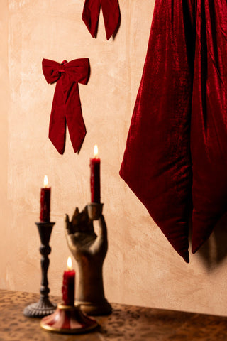 The Red Velvet Bow Christmas Decoration styled on the wall with other bows, above some lit candles on a leopard print table.