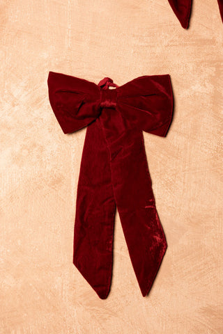 The Red Velvet Bow Christmas Decoration styled on a plain wall.