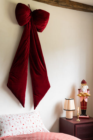The Red Velvet Oversized Bow Decoration on the wall above a bed.
