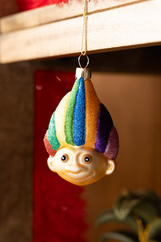 The Retro Troll-Inspired Christmas Tree Decoration hanging from the edge of a wooden shelf.