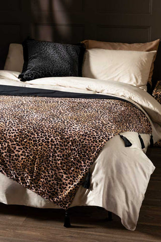 Signature Leopard Print Velvet Throw with Tassels shown on a bed with neutral bedding. 