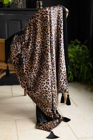 Signature Leopard Print Velvet Throw with Tassels shown draped on a wicker armchair. 