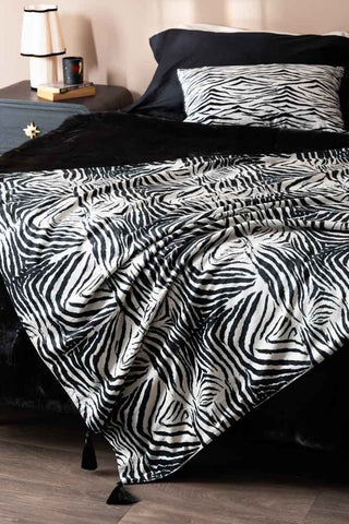 The Zebra Print Velvet Throw with Tassels draped across the end of a bed.
