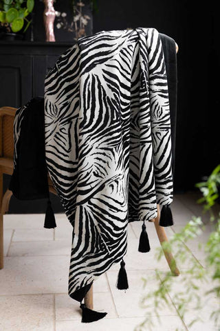 The Zebra Print Velvet Throw with Tassels draped on a wooden chair.
