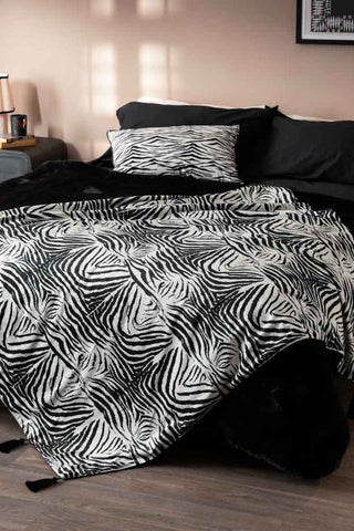 The Zebra Print Velvet Throw with Tassels styled across the end of a bed.
