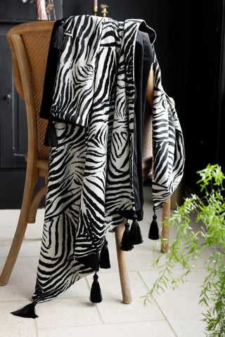 The Zebra Print Velvet Throw with Tassels styled across a wooden dining chair next to a plant.
