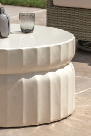 Close-up of the side of theRibbed Edge Round Coffee Table In Ivory, styled with a glass vase and tumbler on top.