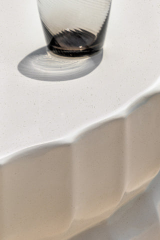 Close-up of the top of the Ribbed Edge Round Coffee Table In Ivory styled with a glass tumbler on.
