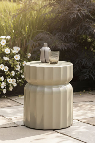 The Ribbed Edge Round Side Table in Ivory Glaze styled outdoors with a vase and a glass tumbler on.