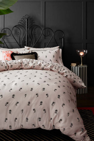 The Rock & Rose Duvet Cover and Pillow Case Set styled on a black bed, with cushions, a rug, bedside table, lamp and books.