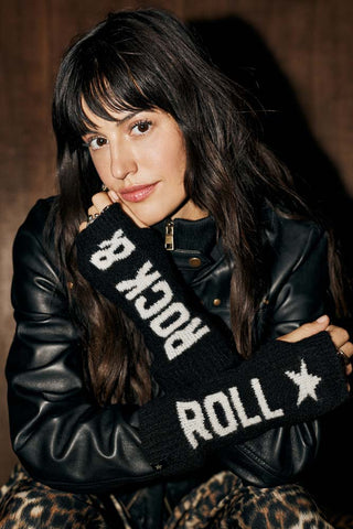 The Rock & Roll Handwarmers are shown worn with a leather jacket and leopard trousers. The design features "rock &" in white lettering against a black ribbed fabric on one side and "roll" with a star in white on the other side, again on a chunky black ribbed fabric. 