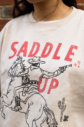Close-up of the design on the Saddle Up Cowboy Sweatshirt in Oat, being worn by a model.