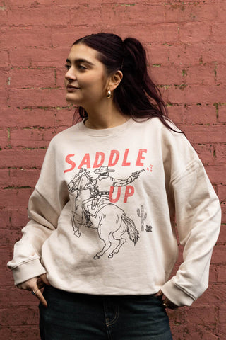 The Saddle Up Cowboy Sweatshirt in Oat worn by a model outdoors.