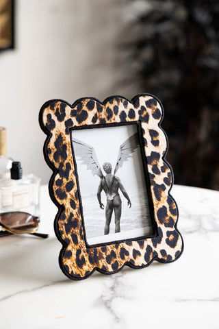 The Scalloped Leopard Print Photo Frame shown on a marble coffee table with a cheeky postcard within the frame. 