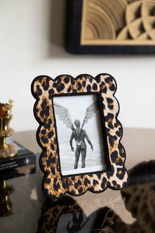 The Scalloped Leopard Print Photo Frame shown on a glass table with a cheeky postcard styled in the frame. 