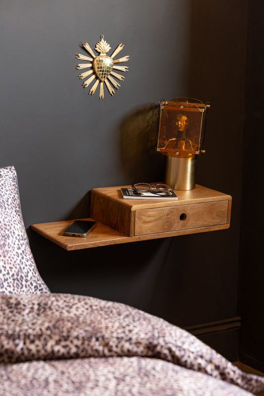 Secret Nook Wall Shelf With Drawer shown styled as a bedside table against a black wall with an amber table lamp. 