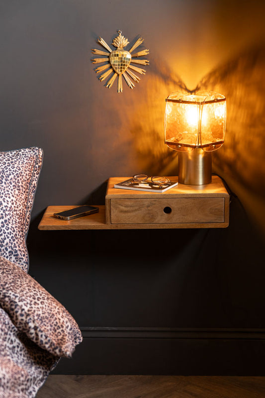 The Secret Nook Wall Shelf With Drawer shown straight on next to a bed with leopard bedding and a black wall. 