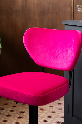A close up image of the Adjustable Bar Stool in Harry's Hot Pink against a textured wood wall. 