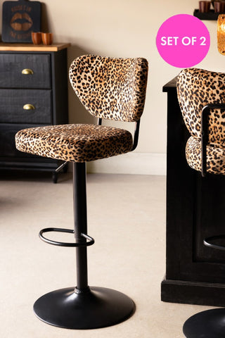 The Set Of 2 Adjustable Bar Stools in Leopard Print Velvet displayed in front of a dark wooden island.