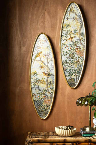 The Set of 2 Framed Oval Chinoiserie Wall Hangings shown together on a textured wood wall. 