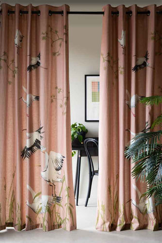 The Set Of 2 Pink Cranes Lined Curtains displayed on a black rail, with a table, chair, plant and art print visible in the background.