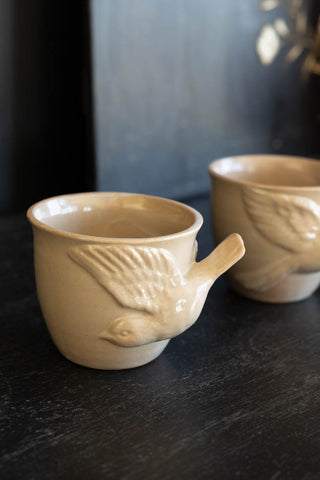 Lifestyle image of the Set Of 2 Taupe Bird Mugs on a black surface