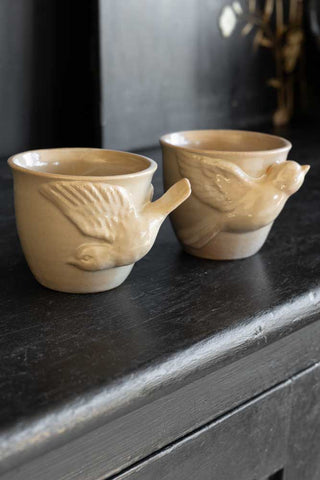 Lifestyle image of the Set Of 2 Taupe Bird Mugs showing both mugs together on black