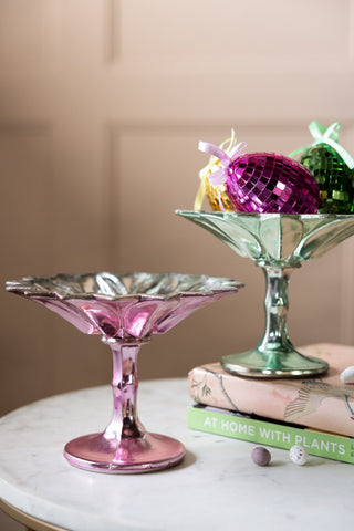 The Set Of 2 Vintage-Style Coloured Glass Display Dishes styled with Easter decorations/chocolates, along with some books.