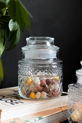 The Set Of 2 Vintage-Style Glass Storage Jars styled with chocolate eggs inside, displayed on a stack of books next to a plant.