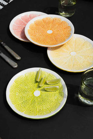 Lifestyle image of all 4 of the Set Of 4 Grapefruit Plates on a black background