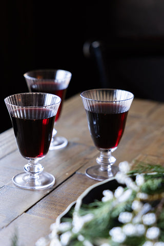 Styled image of the Ribbed Glass Wine Glass on a coaster on wooden surface with dark wall background