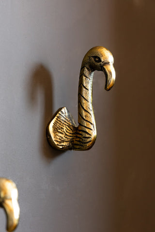A closer view of the Set of 2 Antique Gold Flamingo Head Coat Hooks on a dark wall. 