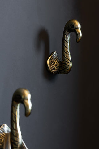 A closer view of the Set of 2 Antique Gold Flamingo Head Coat Hooks on a dark wall. 