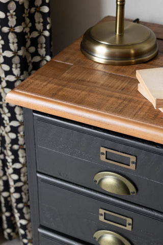 Close-up of the top of a bedside table styled with a lamp and books, with a curtain in the background.