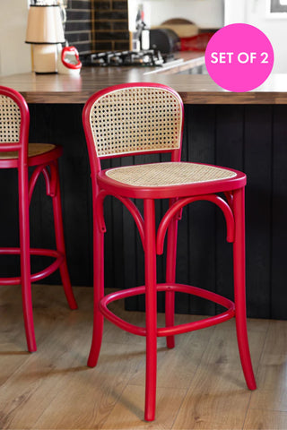 Two of the Chez Pitou Wood & Woven Cane Bar Stool in Red styled in a kitchen in front of a breakfast bar.