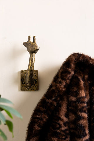 The Set of 2 Gold Giraffe Coat Hooks on a wall, one with a leopard print coat on, styled with some greenery in the corner of the frame.