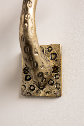 Close-up of the back plate of one of the Set of 2 Gold Giraffe Coat Hooks, on a white wall.