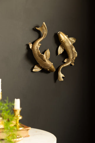 The Set of 2 Gold Koi Fish Wall Art styled on a black wall above a table with some accessories on.